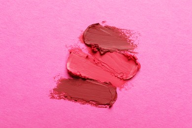 Smears of beautiful lipsticks on pink background, top view