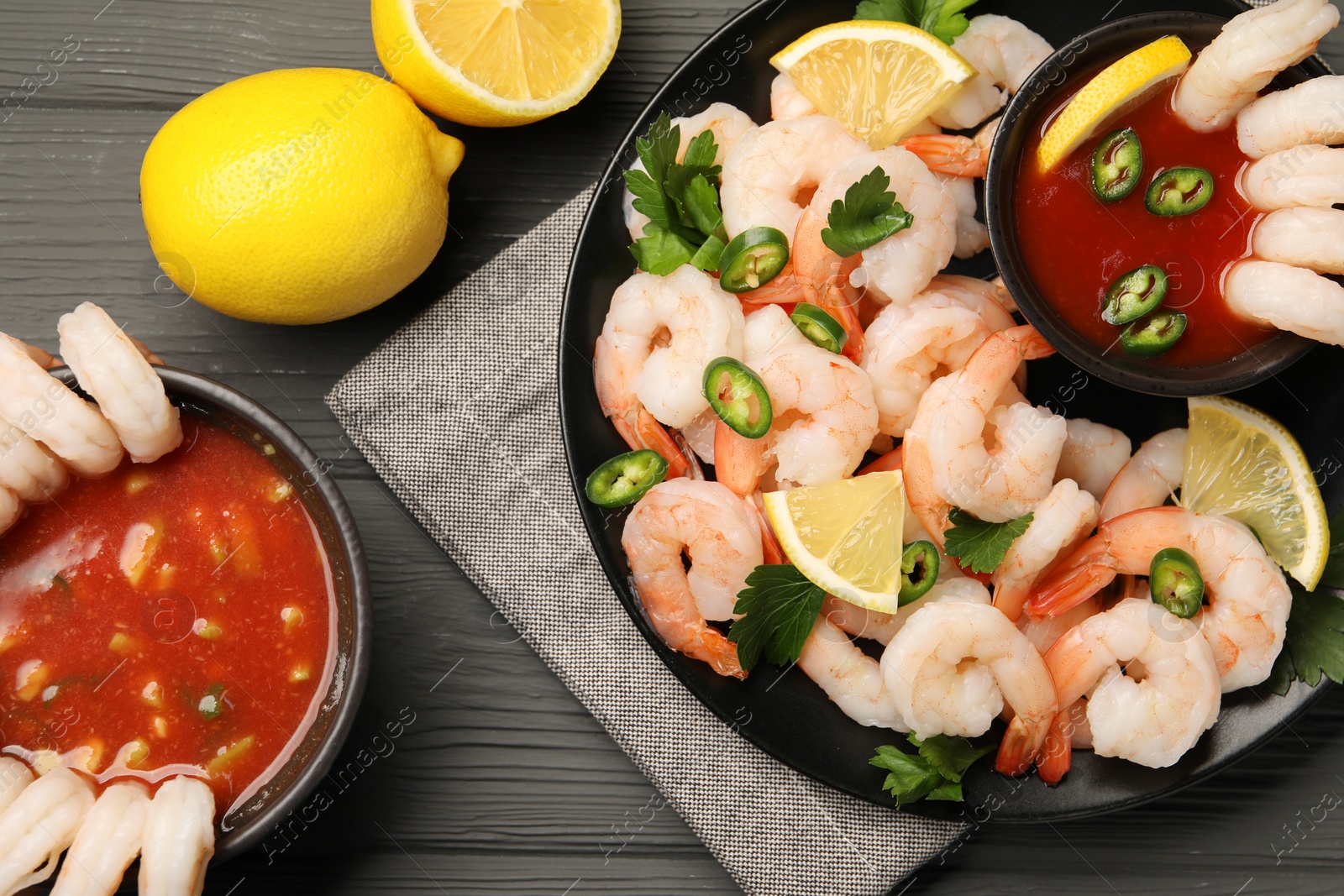 Photo of Tasty boiled shrimps with cocktail sauce, chili, parsley and lemon on grey wooden table, flat lay