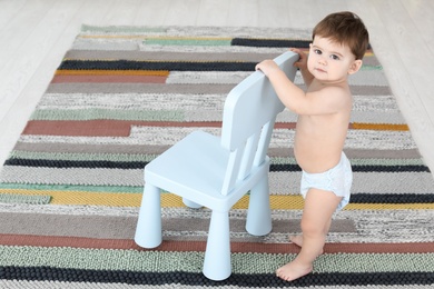 Photo of Cute baby holding on to chair at home.  Learning to walk