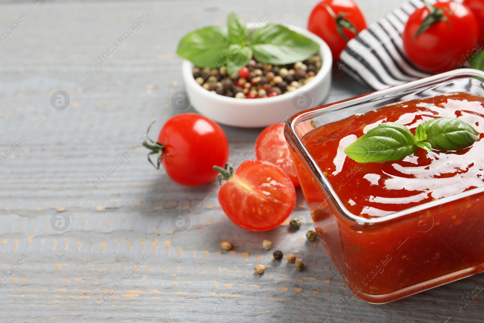 Photo of Spicy chili sauce with basil on grey wooden table, closeup. Space for text