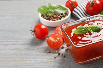 Photo of Spicy chili sauce with basil on grey wooden table, closeup. Space for text