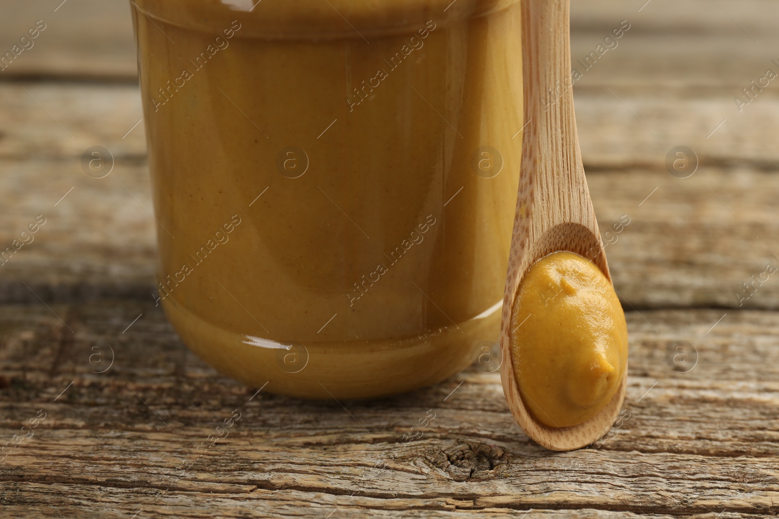 Photo of Jar and spoon with tasty mustard sauce on wooden table, closeup