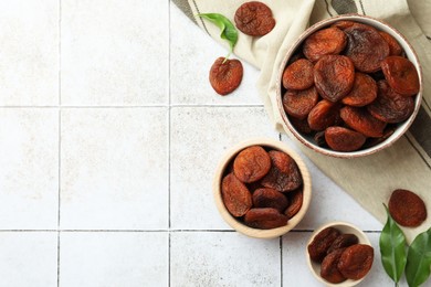 Tasty apricots, green leaves and space for text on white tiled table, flat lay. Dried fruits