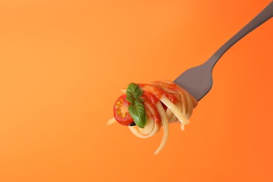 Photo of Tasty pasta with tomato sauce and basil on fork against orange background, space for text