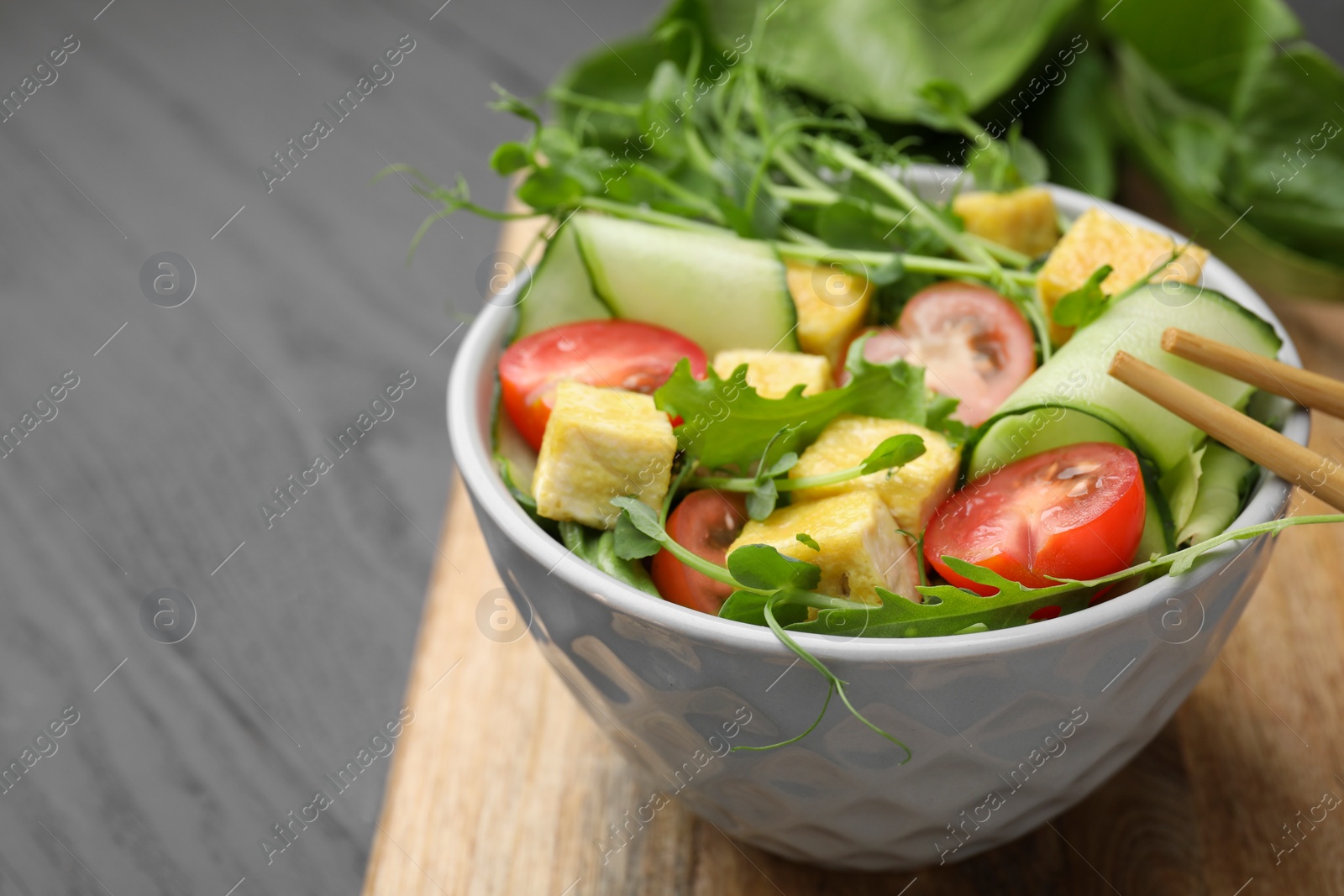 Photo of Bowl of tasty salad with tofu and vegetables on grey wooden table, closeup. Space for text