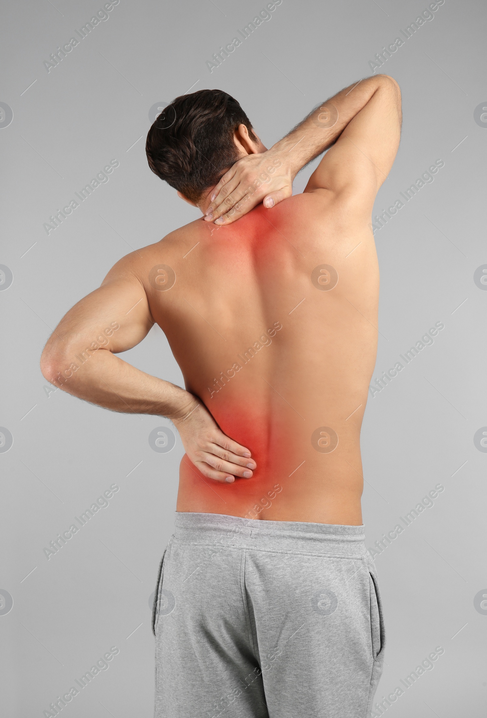 Image of Young man suffering from back pain on grey background