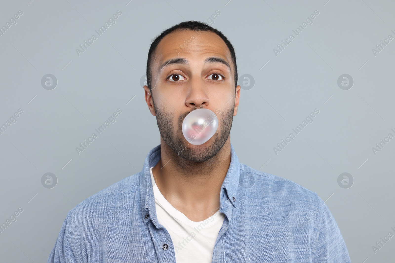 Photo of Portrait of young man blowing bubble gum on light grey background