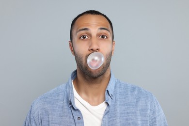 Portrait of young man blowing bubble gum on light grey background