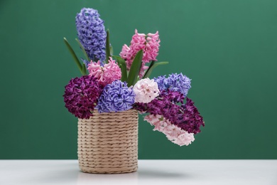 Photo of Beautiful hyacinths in wicker pot on table against color background, space for text. Spring flowers