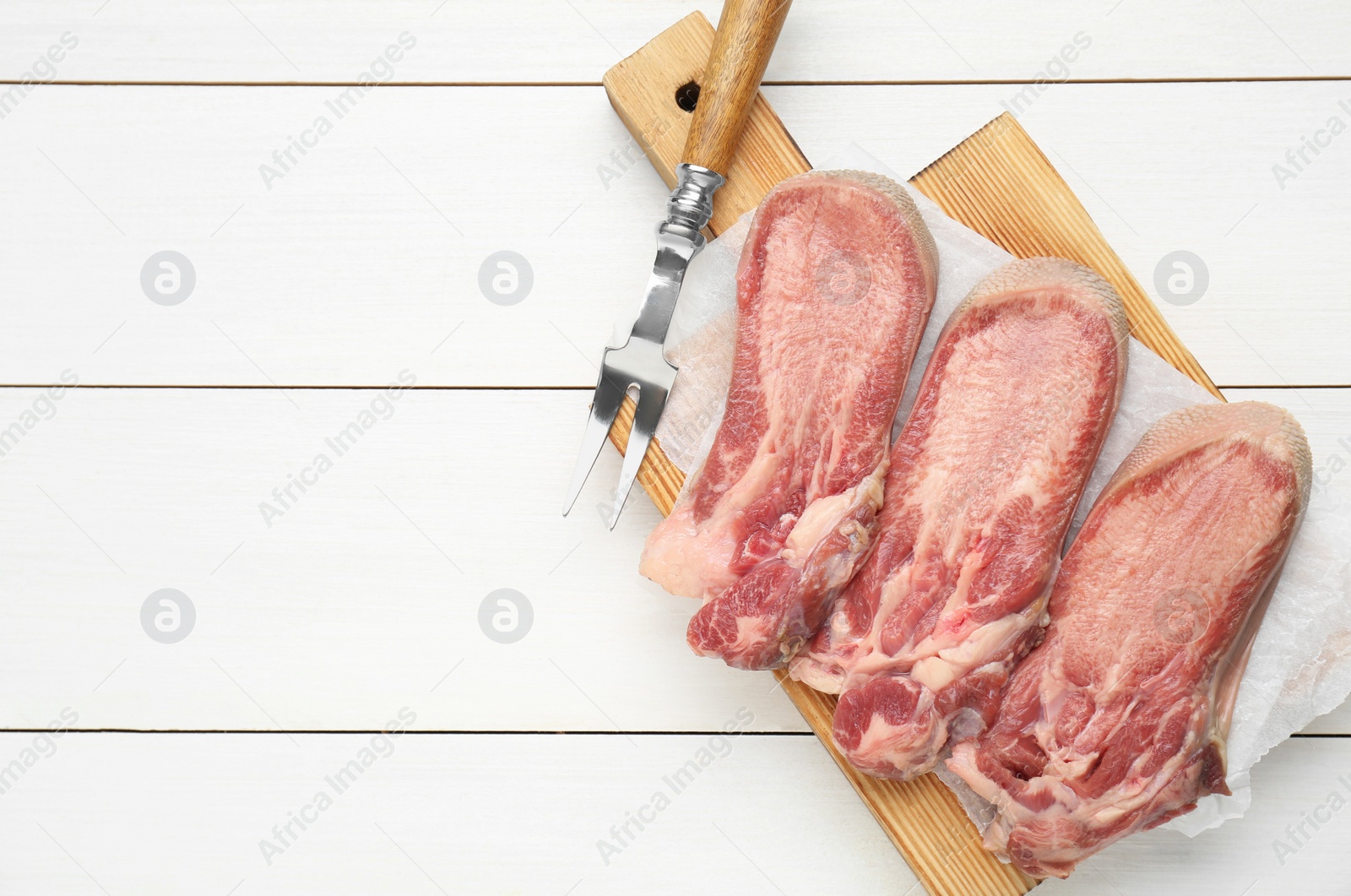 Photo of Raw beef tongue pieces and carving fork on white wooden table, top view. Space for text
