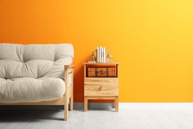 Stylish beige sofa and small wooden table near orange wall indoors. Interior design