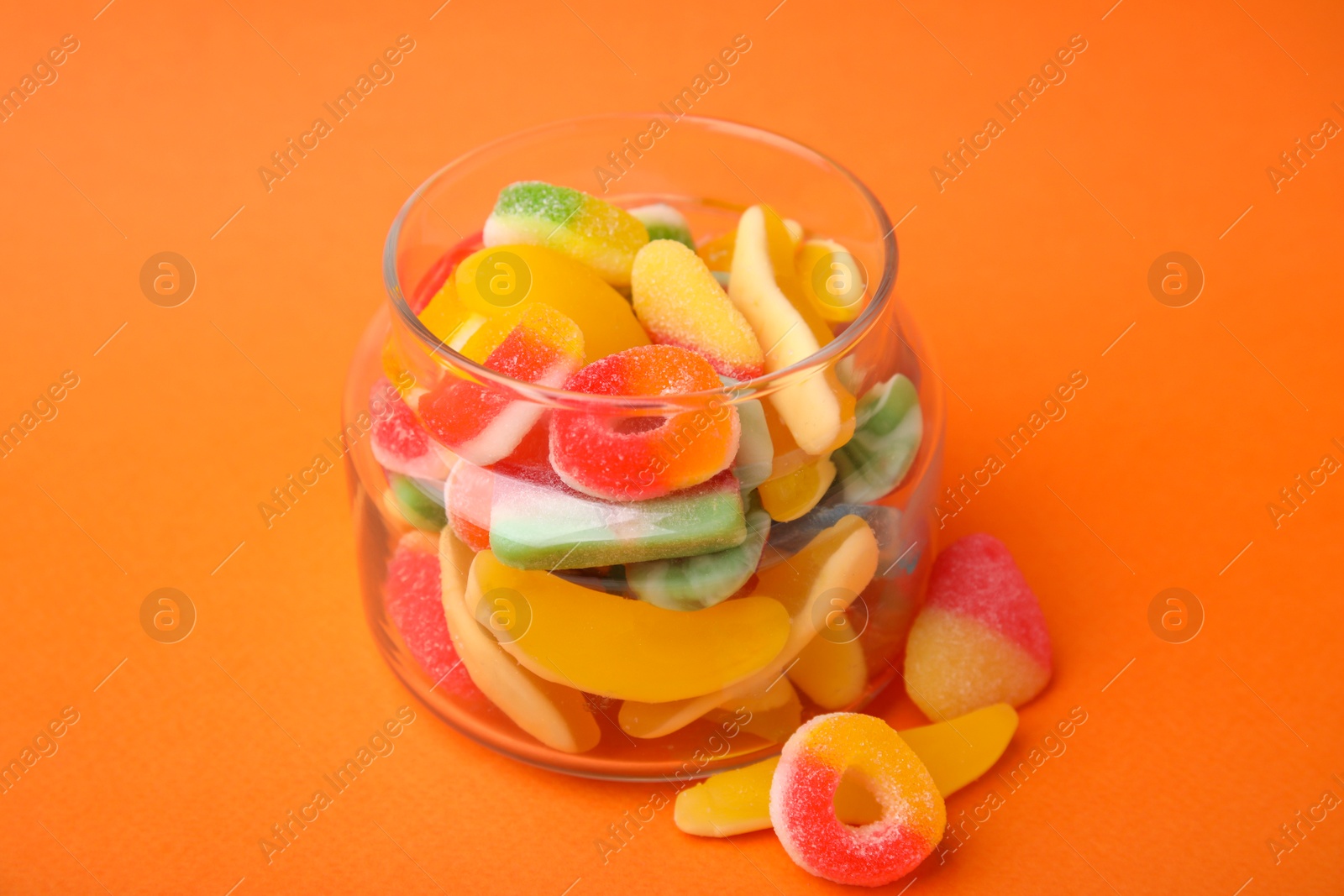 Photo of Tasty jelly candies in jar on orange background, closeup