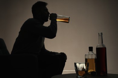 Photo of Addicted man drinking alcohol indoors, focus on table with bottles