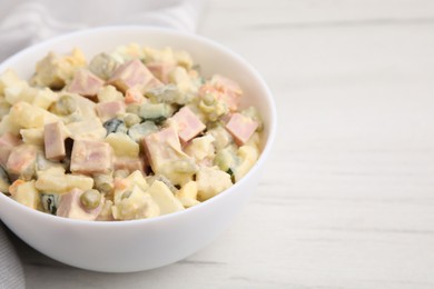 Photo of Tasty Olivier salad with boiled sausage in bowl on white table, closeup. Space for text