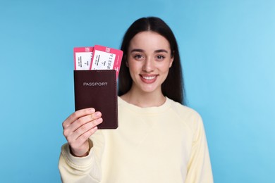 Photo of Happy woman showing passport and tickets on light blue background, selective focus