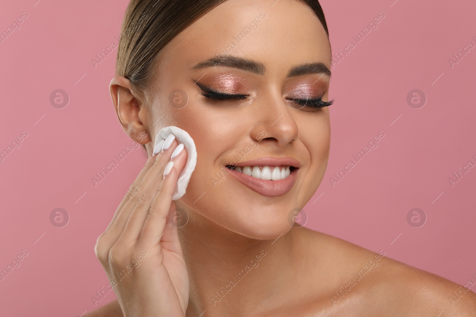 Photo of Beautiful woman removing makeup with cotton pad on pink background, closeup