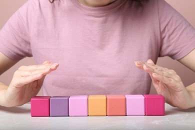 Woman demonstrating empty colorful cubes at grey marble table, closeup. Space for design