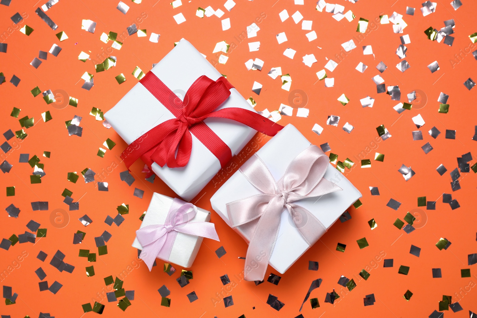 Photo of Different gift boxes and confetti on orange background, flat lay