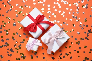 Photo of Different gift boxes and confetti on orange background, flat lay