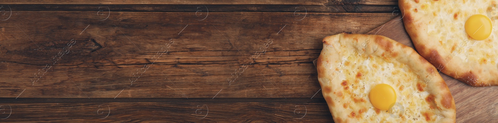 Image of Delicious Adjarian khachapuris on wooden table, flat lay. Banner design with space for text