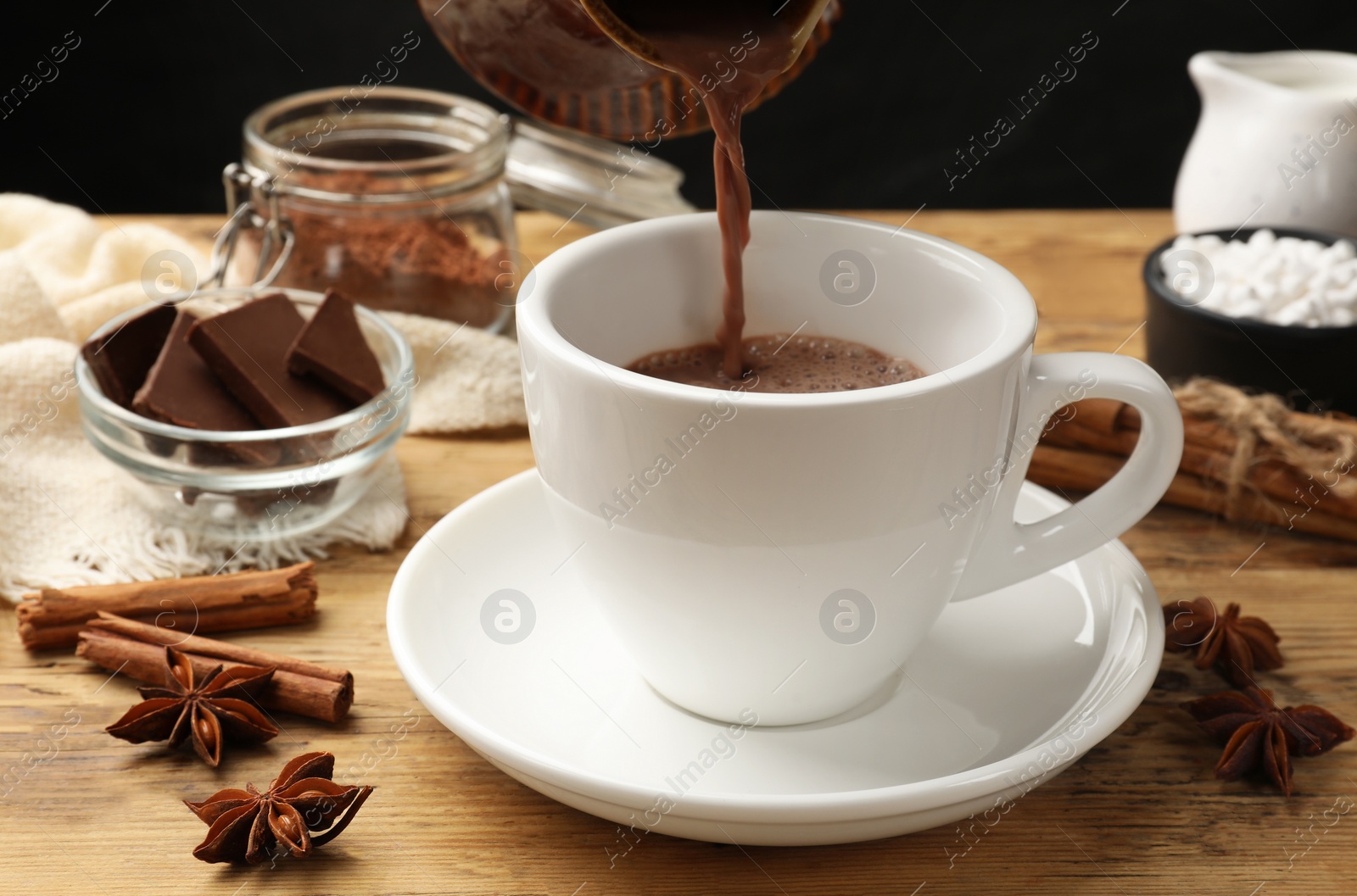 Photo of Pouring tasty hot chocolate into cup at wooden table, closeup