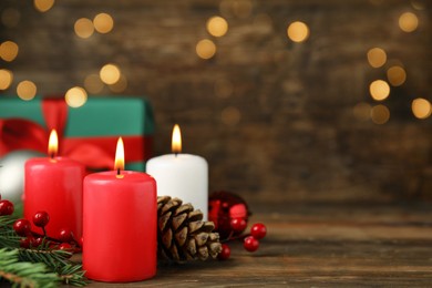 Burning candles, gift box and Christmas decor on wooden table, bokeh effect. Space for text