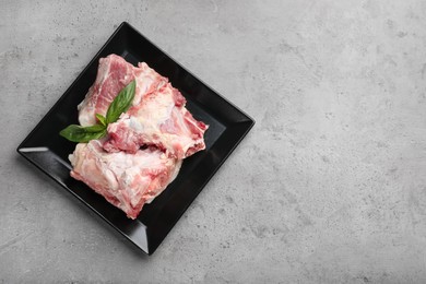 Plate with raw chopped meaty bones and basil on grey table, top view. Space for text