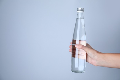 Photo of Woman holding glass bottle with water on white background, closeup. Space for text
