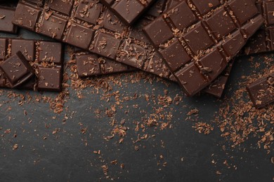 Photo of Pieces and shavings of tasty chocolate bars on dark grey table, flat lay. Space for text