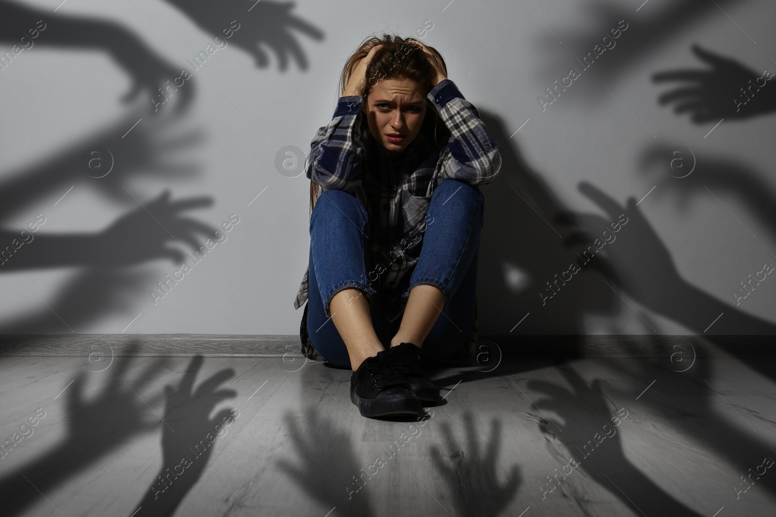 Image of Paranoid delusion. Scared woman sitting near wall. Shadows of hands reaching for her symbolizing fear and anxiety