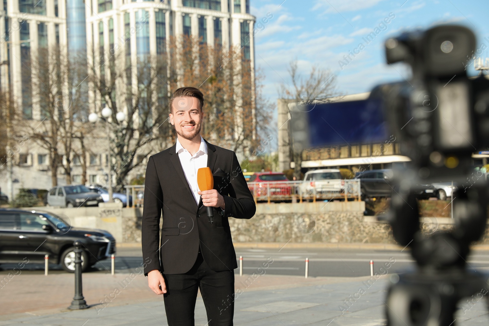 Photo of Young male journalist with microphone working on city street