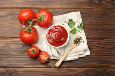 Photo of Delicious ketchup in bowl, tomatoes, parsley and peppercorns on wooden table, top view