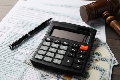 Tax law. Forms, dollar banknotes, calculator and gavel on wooden table, closeup