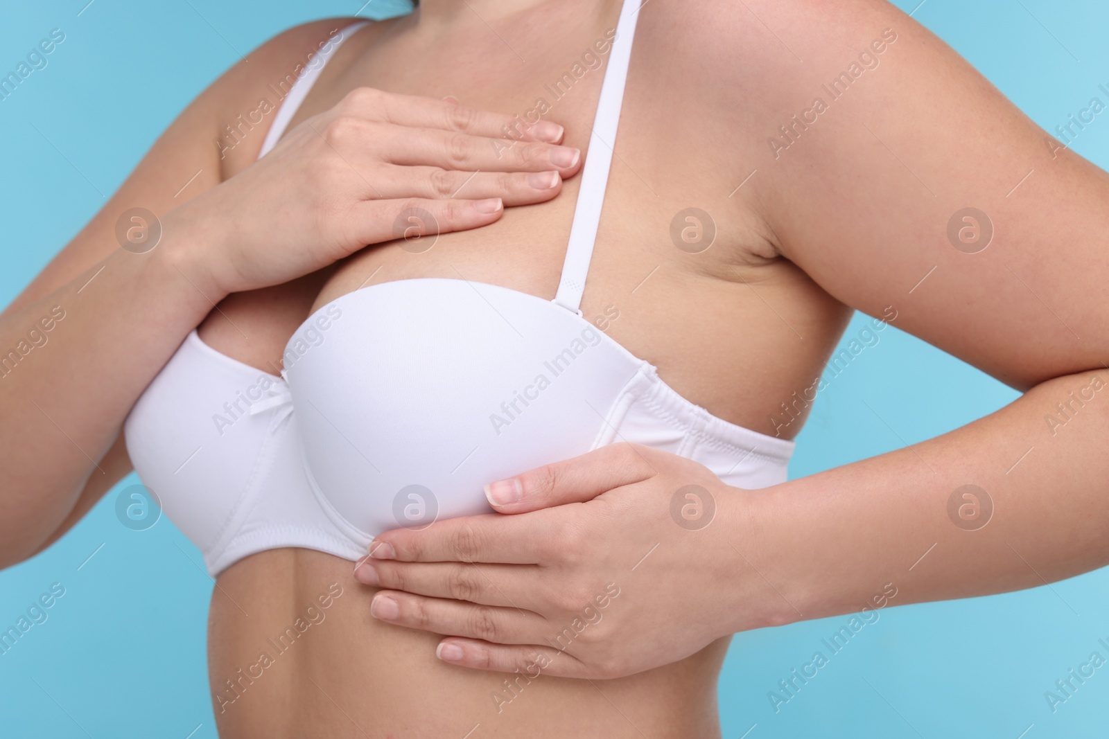 Photo of Mammology. Woman in bra doing breast self-examination on light blue background, closeup
