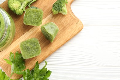 Photo of Frozen broccoli puree cubes and fresh broccoli on white wooden table, flat lay. Space for text
