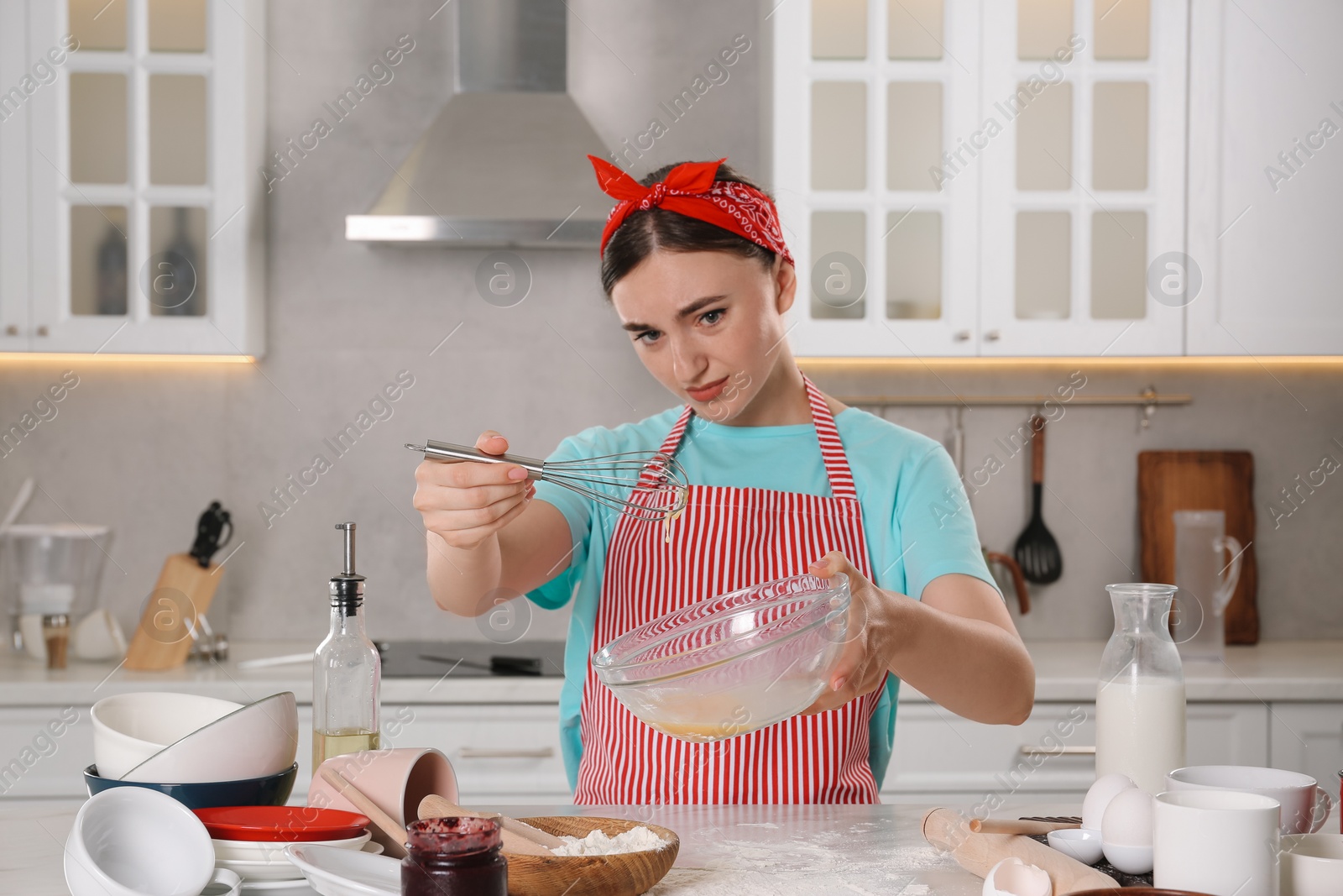 Photo of Beautiful woman cooking in messy kitchen. Many dishware, utensils and scattered flour on countertop
