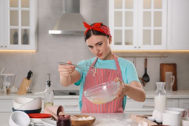 Beautiful woman cooking in messy kitchen. Many dishware, utensils and scattered flour on countertop