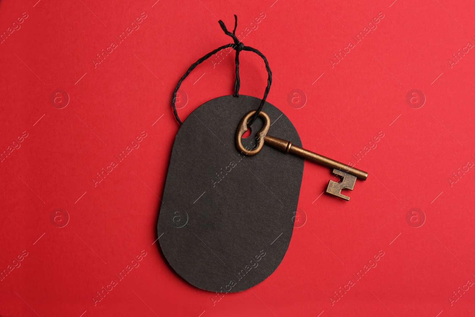 Photo of Vintage key with blank tag on red background, top view. Keyword concept