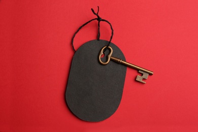 Photo of Vintage key with blank tag on red background, top view. Keyword concept