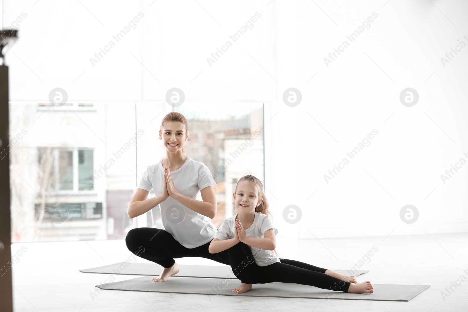 Photo of Mother and daughter in matching sportswear doing yoga together at home