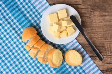 Photo of Tasty cut baguette with fresh butter on wooden table, flat lay