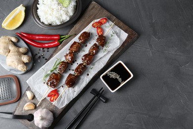 Skewers with pieces of tasty chicken meat glazed in soy sauce and other products on grey textured table, flat lay. Space for text