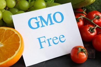 Photo of Tasty fresh GMO free products and paper card on black table, closeup