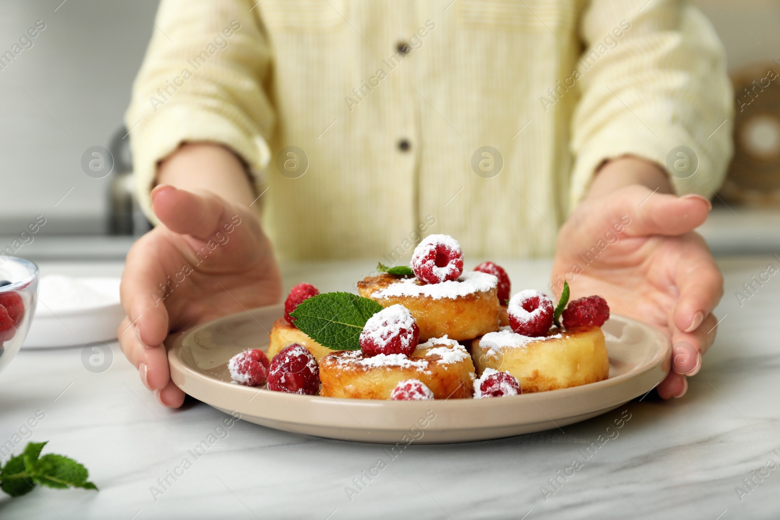 Photo of Woman with plate of delicious cottage cheese pancakes at white table, closeup