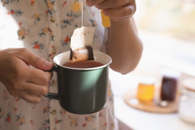 Photo of Woman taking tea bag out of cup indoors, closeup