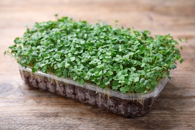 Fresh organic microgreen in plastic container on wooden table, closeup