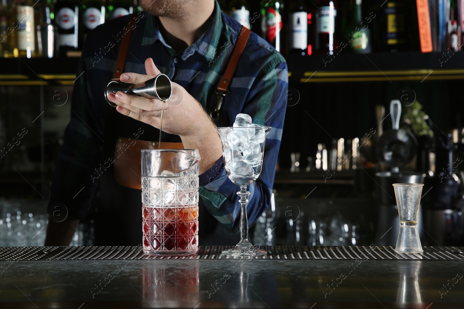 Photo of Barman pouring cocktail ingredients into mixing glass at counter in pub, closeup