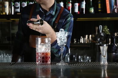 Barman pouring cocktail ingredients into mixing glass at counter in pub, closeup