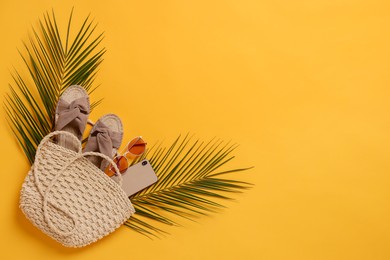 Photo of Wicker bag, smartphone, palm leaves and beach accessories on orange background, flat lay. Space for text