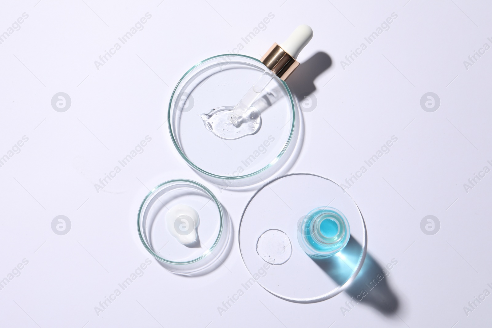 Photo of Petri dishes with samples of cosmetic serums, bottle and pipette on white background, flat lay